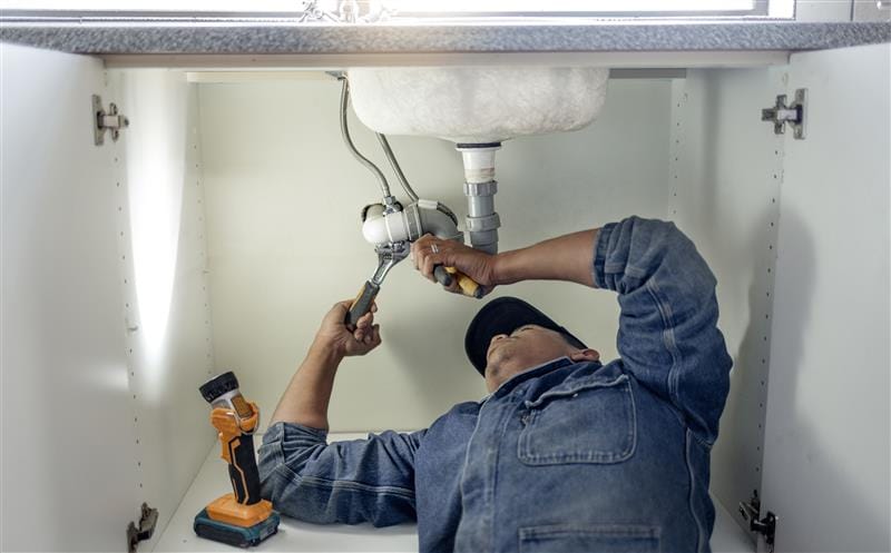 Plumber repairing pipes beneath a bathroom sink in Diamond Bar